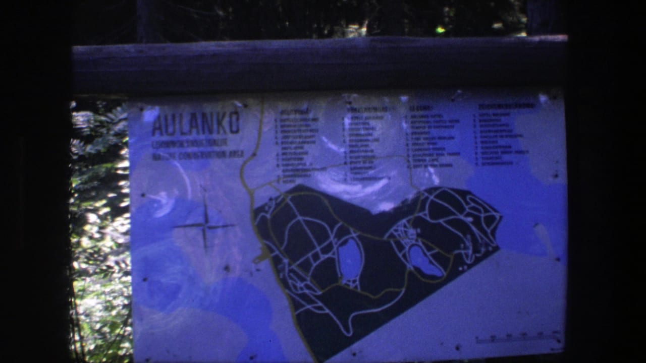 Outdoor Aulanko map board with printed trails, text columns, rails, and trees behind it.