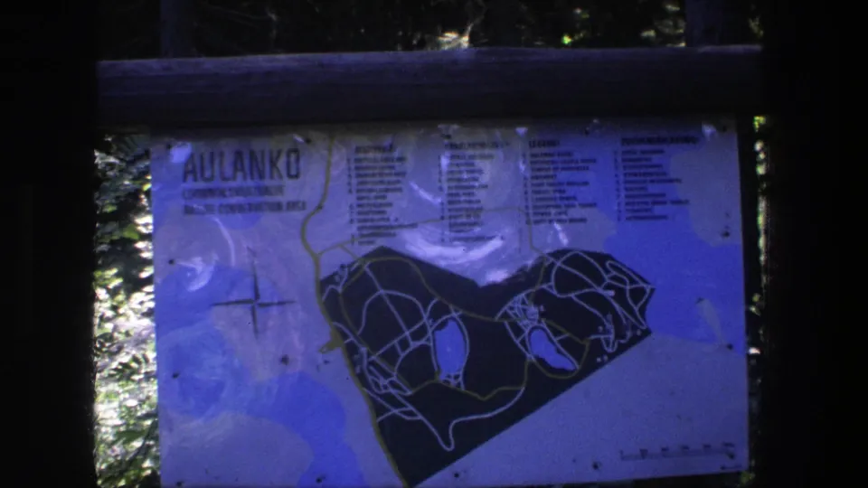 Blue-tinted 8mm frame showing the Aulanko park sign and map, with rails crossing the foreground and trees beyond.