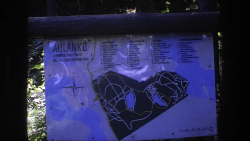 Final 1975 8mm frame of the Aulanko sign, with the park map, text columns, wooden rails, and shaded trees visible.