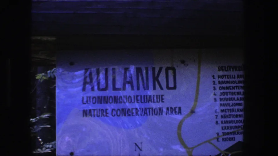 1970s 8mm frame showing a close view of an Aulanko Nature Conservation Area sign with Finnish and English text.