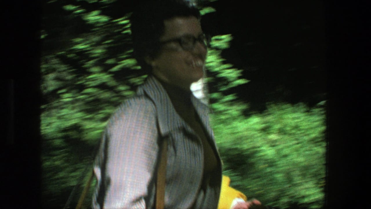 The woman moves past the handheld camera in a Danish forest, with motion blur and bright green foliage behind her.