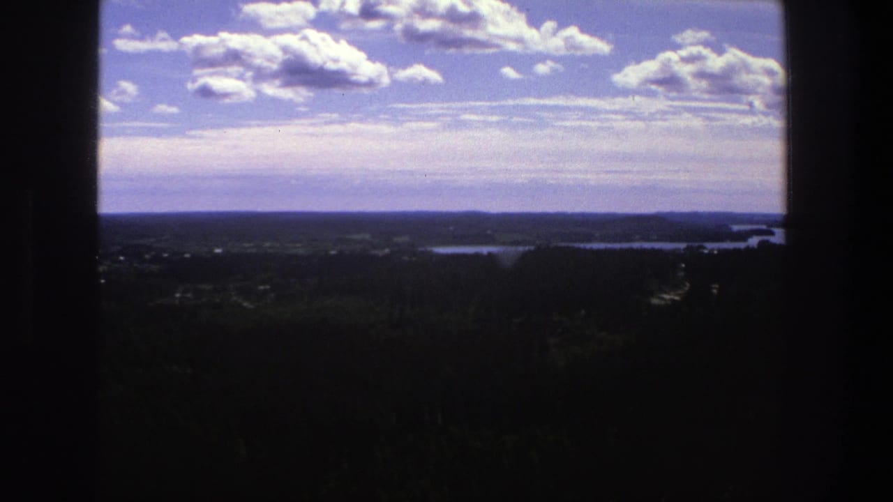 Distant forest and water under blue sky, seen through dark frame edges.