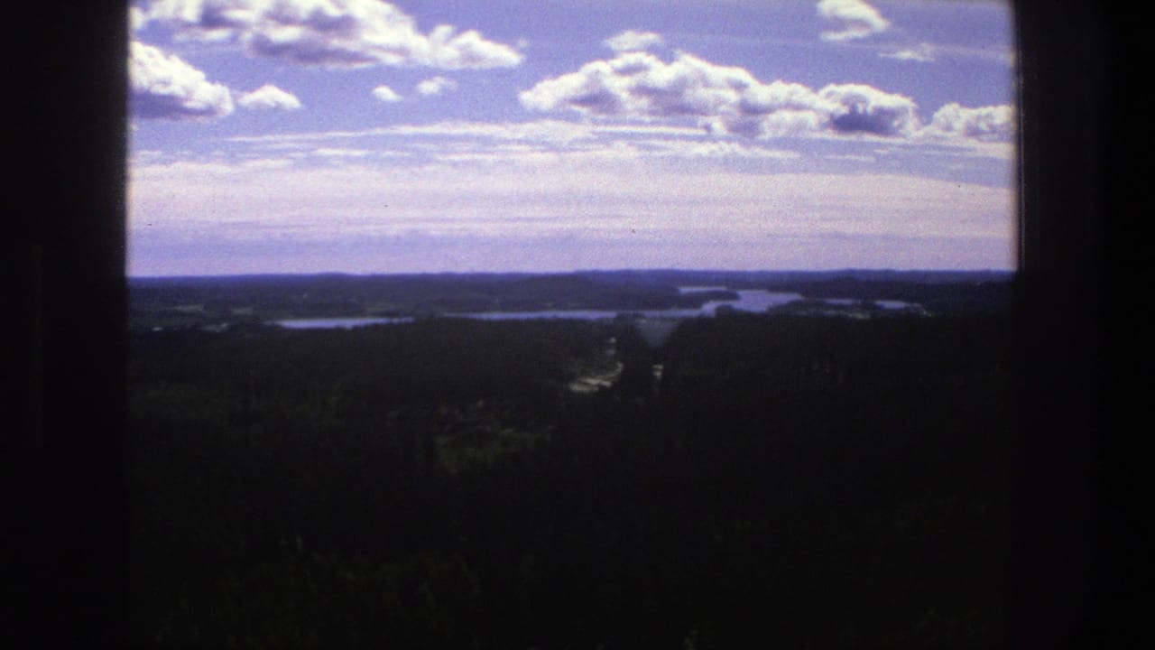 Wide landscape view with clouds, distant water, forested land, and dark vertical framing.
