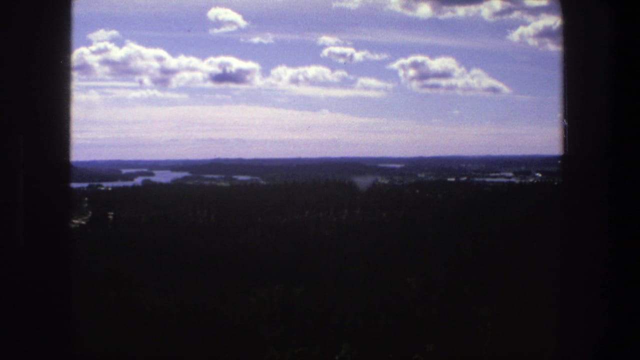Scattered bright clouds over a wide, dark landscape with water on the horizon.