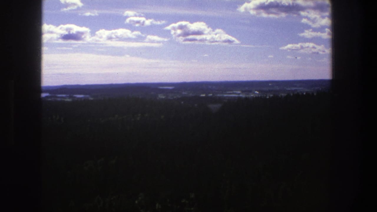Wide forested landscape under a partly cloudy sky with dark vertical framing edges.