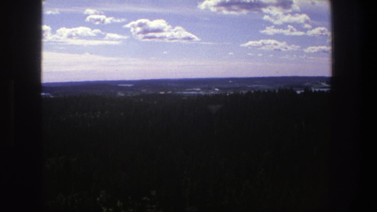 Distant hills and forest beneath scattered clouds, framed by dark vertical edges.