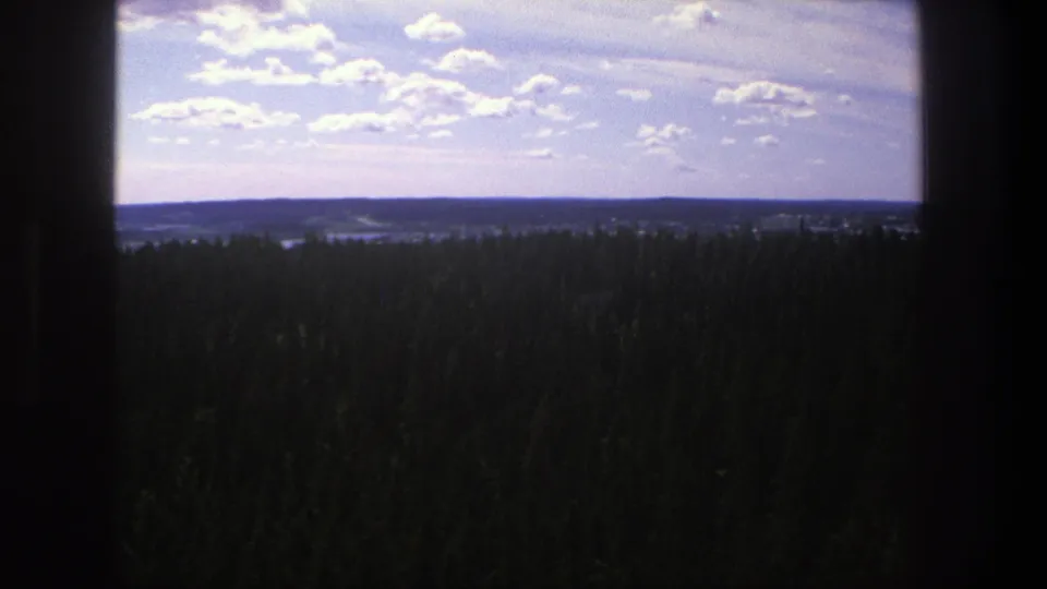 1975 Denmark home-movie still showing a dark foreground frame around treetops, distant landscape, and sunlit clouds.
