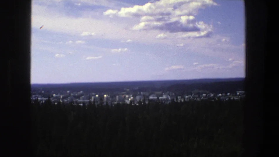 1975 Danish home-movie view of a distant town and forested foreground under a cloud-dappled sky.