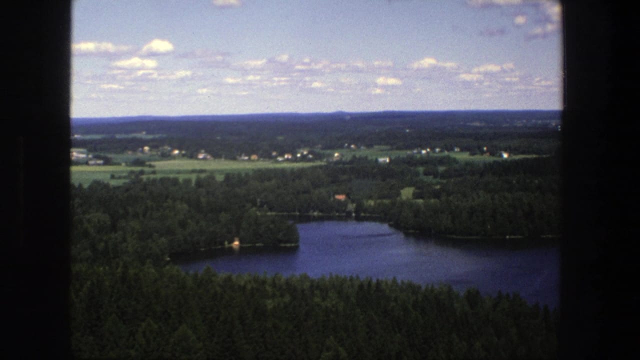 Wide countryside view with a lake at right, forest below, fields, and scattered clouds.