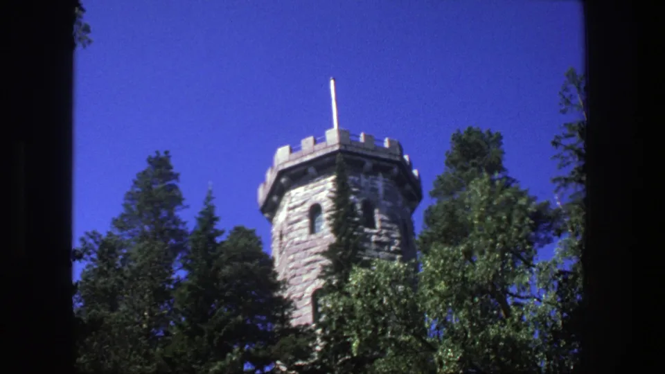 1975 Denmark 8mm frame showing a stone observation tower with crenellations and a flagpole against a vivid blue sky.
