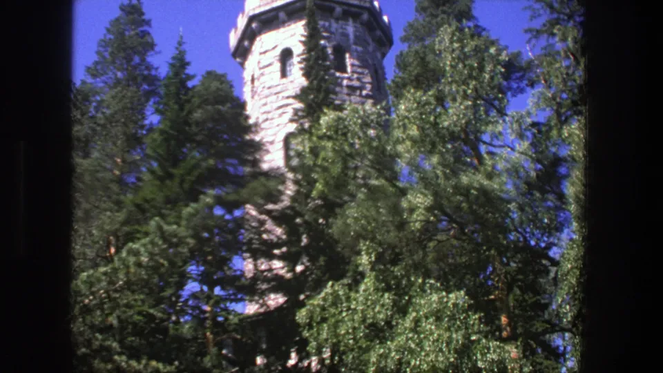 1975 Denmark 8mm frame with a round stone tower, arched openings, and foliage filling the foreground.