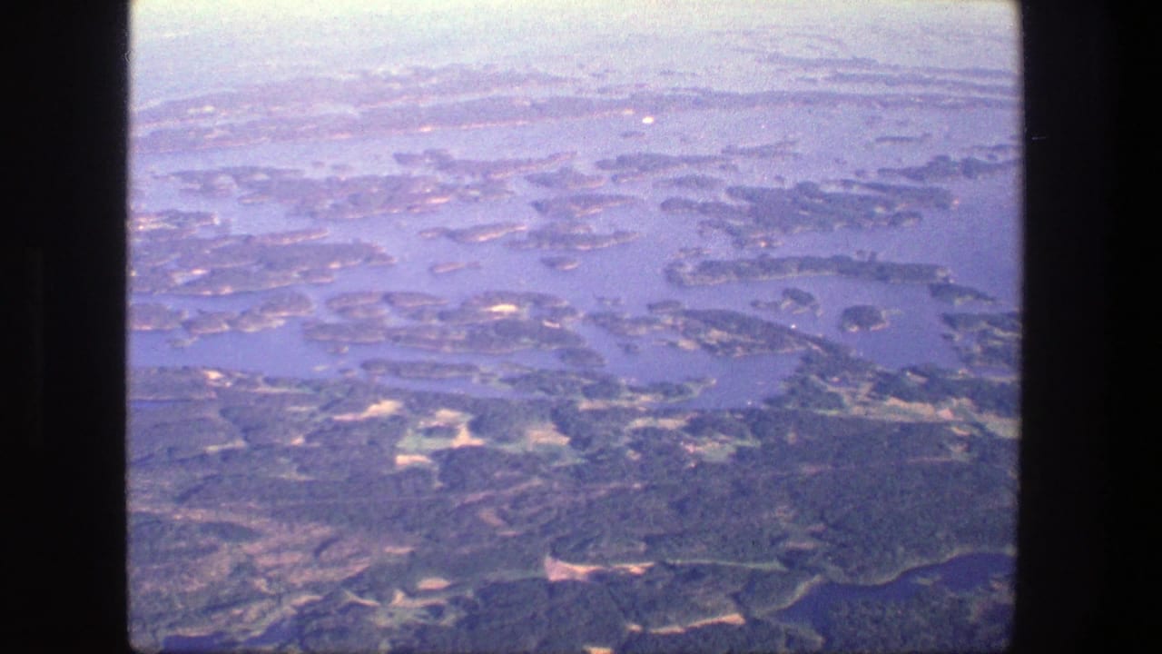 Aerial 8mm view over Denmark, with scattered islands, channels, wooded land, and pale haze across the horizon.