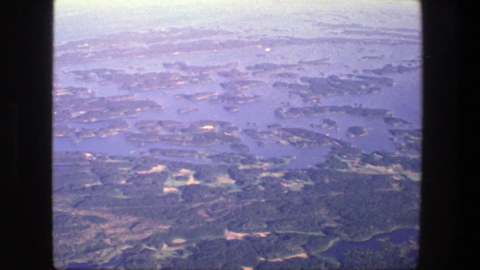 Aerial 8mm view over Denmark, with scattered islands, channels, wooded land, and pale haze across the horizon.