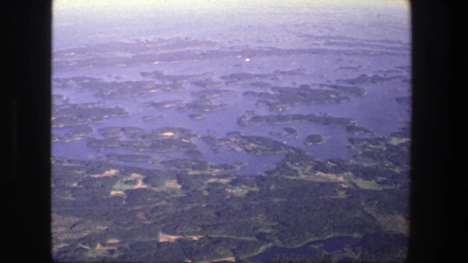 Soft 8mm aerial frame over Danish island waters, showing irregular shorelines, wooded terrain, and a darker lake or inlet near the lower edge.