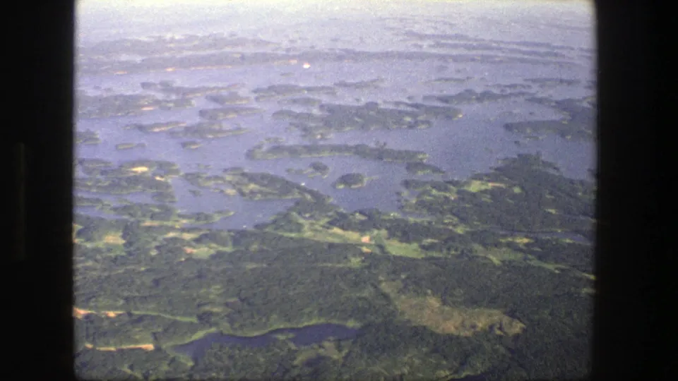 1975 Denmark aerial frame showing green forest, blue water channels, island shorelines, and soft color-shifted 8mm texture.