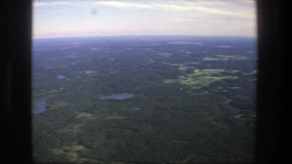The final 1975 Denmark aerial frame shows green woodland, scattered lakes, and open patches receding toward a pale horizon.