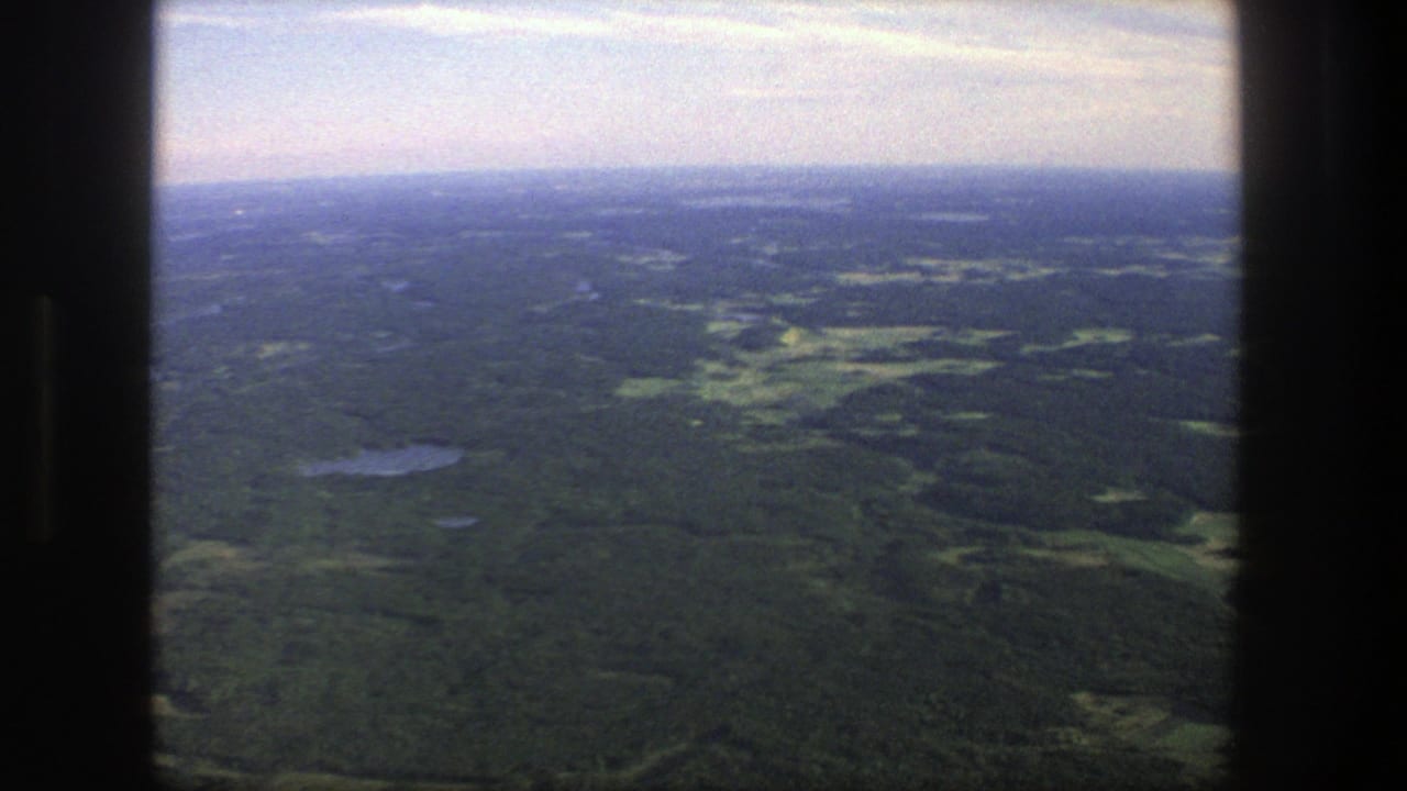 Aerial landscape of forest, small lakes, and open fields under a hazy sky.