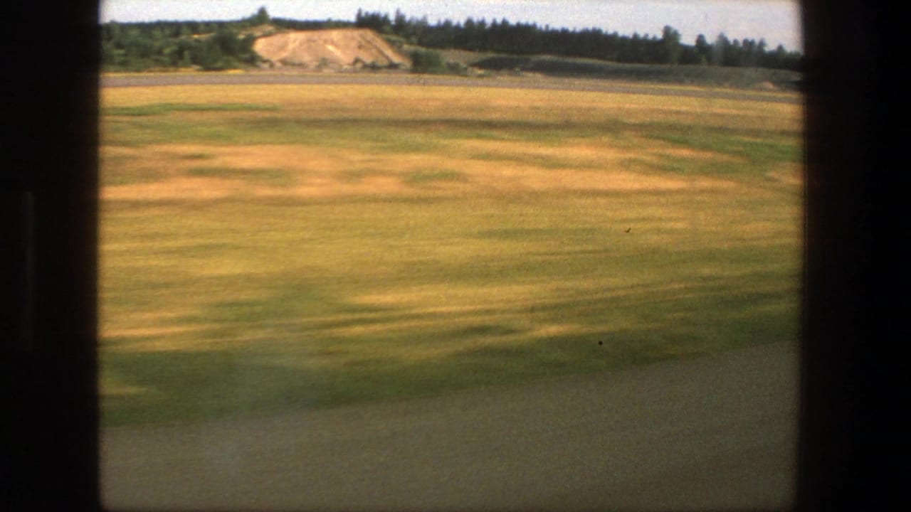 Open field with distant trees and pale earthwork beyond the road.