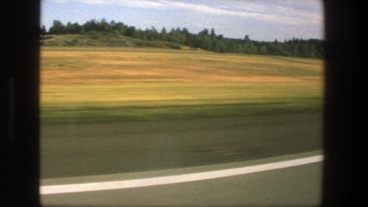 Road edge and open fields seen through a moving vehicle window.