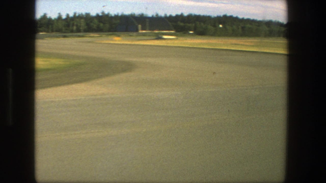 Runway and grassy field with distant hangar-like structures beyond the airfield.