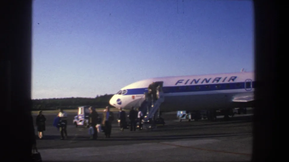 1975 Denmark tarmac scene with visible passengers boarding a Finnair jet by mobile stairs beneath a clear blue sky.