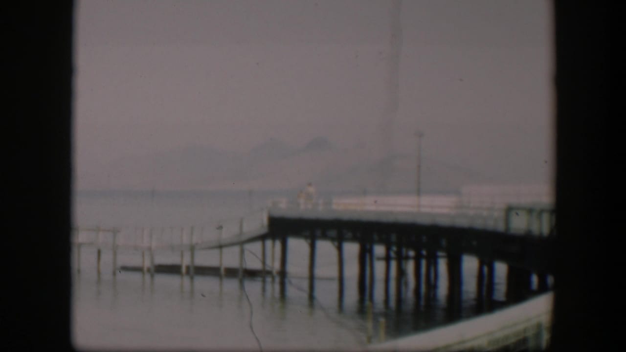 1951 Wyoming 8mm frame showing a wooden pier over still water, with fog or haze softening distant mountains.