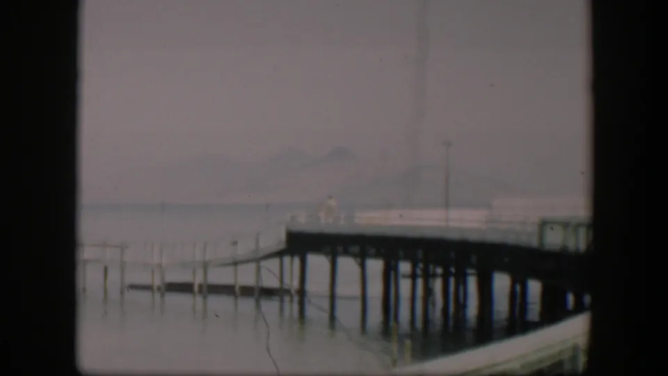 1951 Wyoming 8mm frame showing a wooden pier over still water, with fog or haze softening distant mountains.