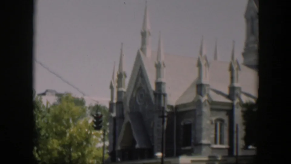 1951 Wyoming 8mm frame showing a stone church facade with steep gables, pointed spires, trees, and a street signal.