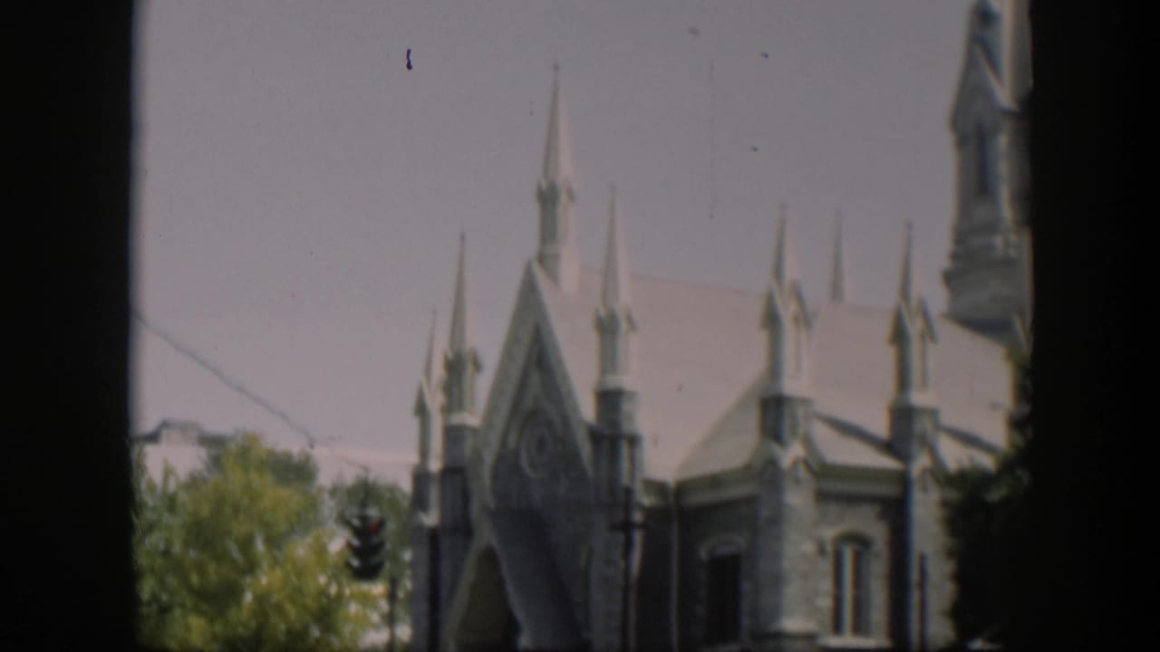 1951 Wyoming 8mm frame showing a stone church exterior with Gothic-style spires, trees, a traffic light, and dark frame edges.