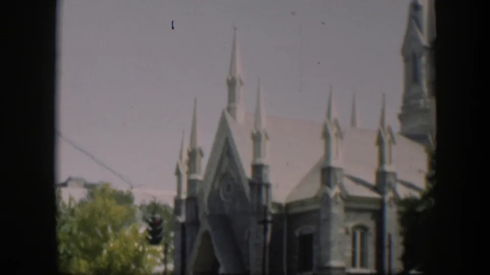 1951 Wyoming 8mm frame showing a stone church exterior with Gothic-style spires, trees, a traffic light, and dark frame edges.