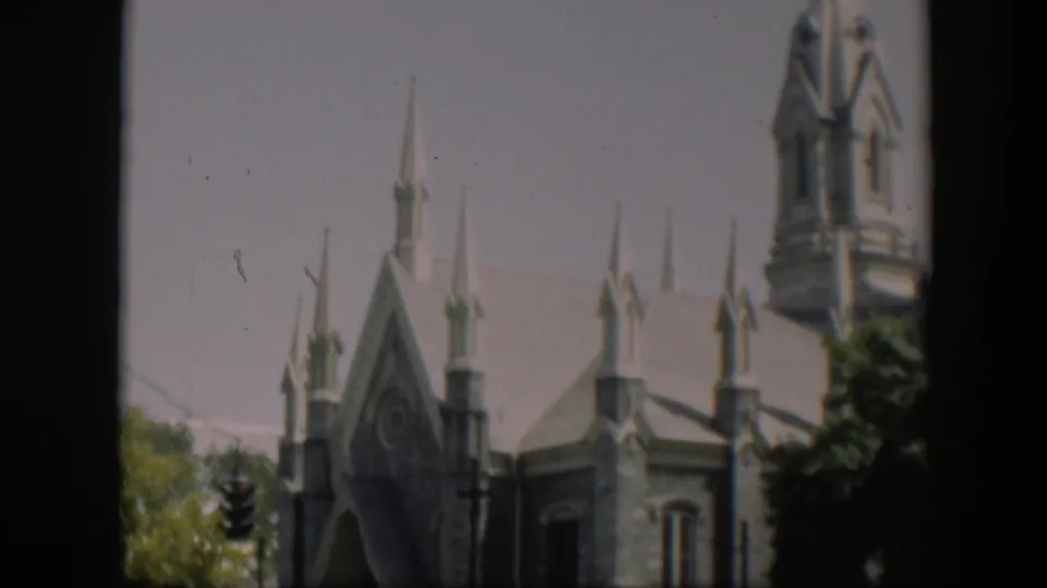 1951 Wyoming home-movie frame showing the church roofline, pointed spires, trees, and a dark vertical border from the film frame.