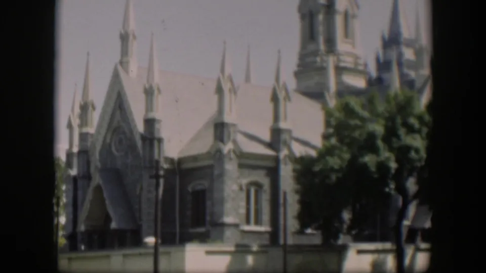 1951 Wyoming 8mm frame showing a Gothic-style church exterior, arched entrance, spires, trees, and a traffic signal in front.