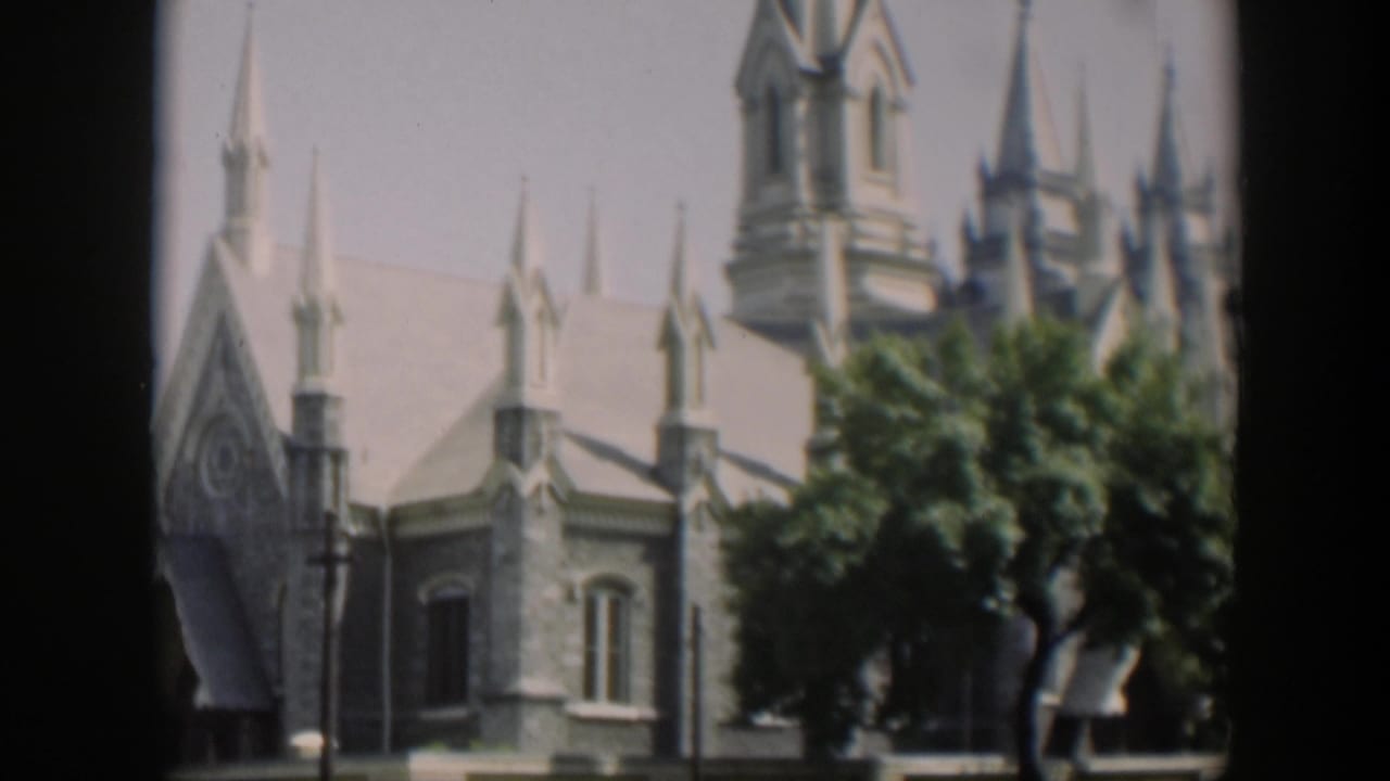 Cropped view of a large light stone building with spires and trees in front.