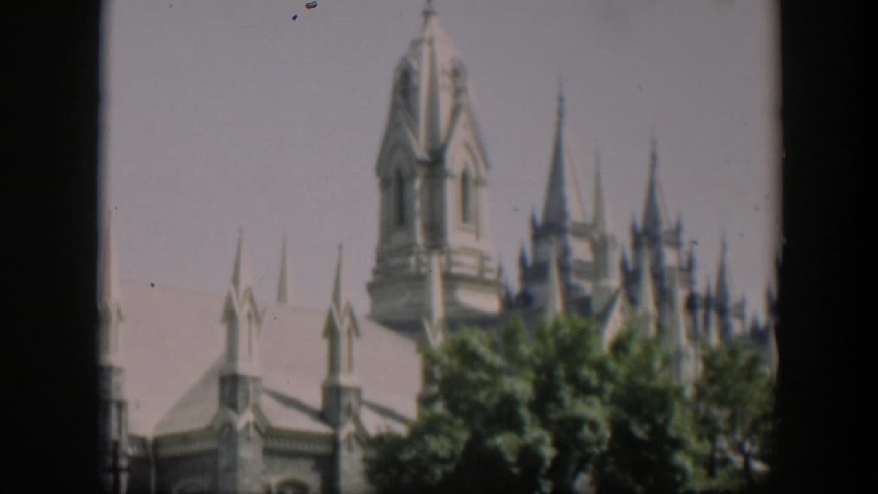 Upper section of a turreted stone building rising above leafy trees.