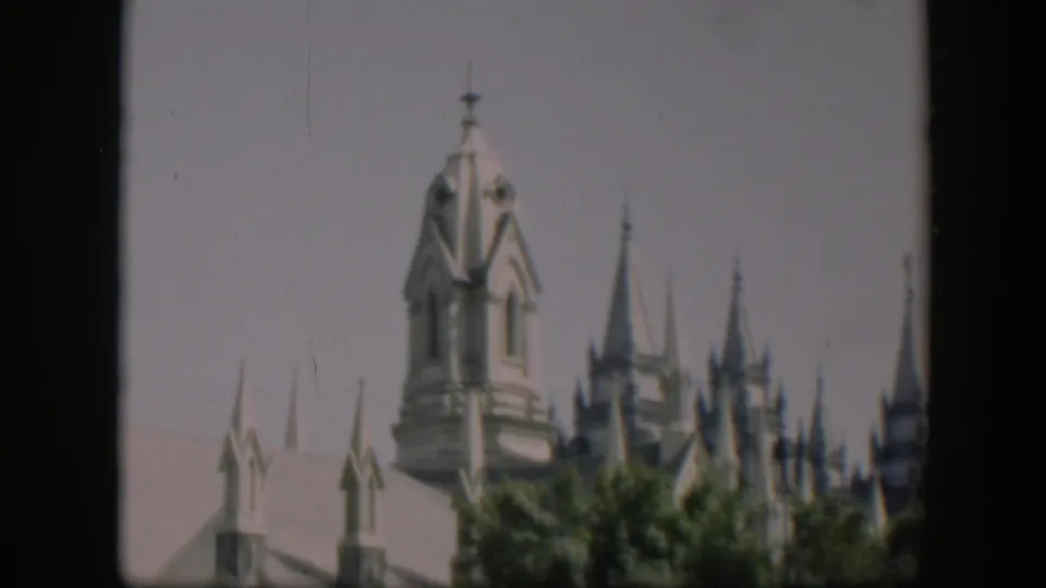 1951 Wyoming 8mm frame emphasizing a Gothic-style turret, narrow spires and treetops in front of the building.
