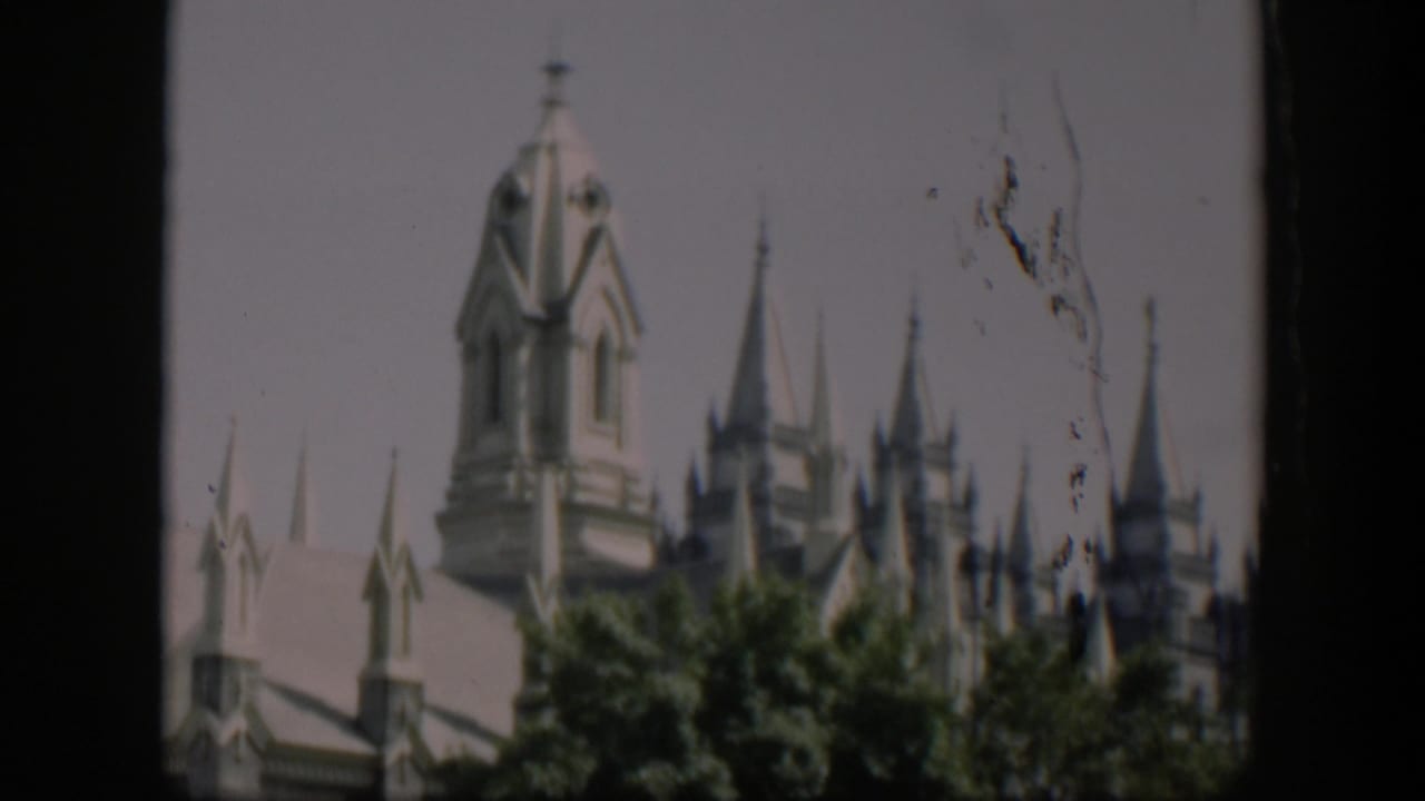 White castle-like building with spires partly hidden by trees.