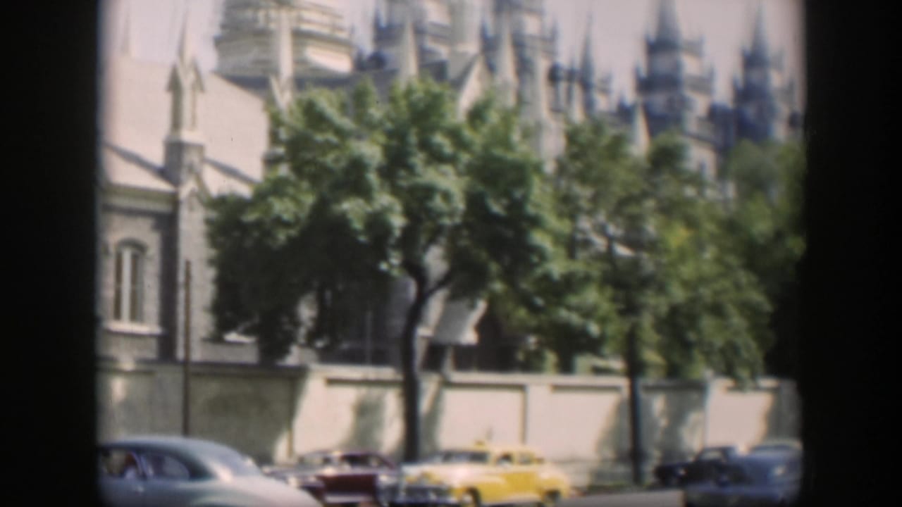 1951 Wyoming street view with a yellow car, other mid-century vehicles, trees, and a tan building with pointed spires.