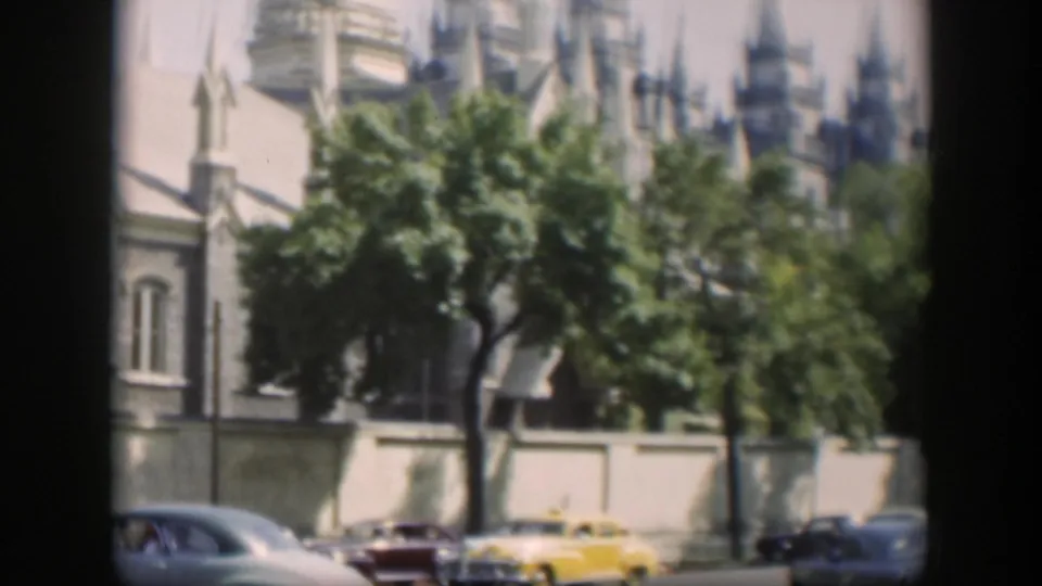 1951 Wyoming street view with a yellow car, other mid-century vehicles, trees, and a tan building with pointed spires.