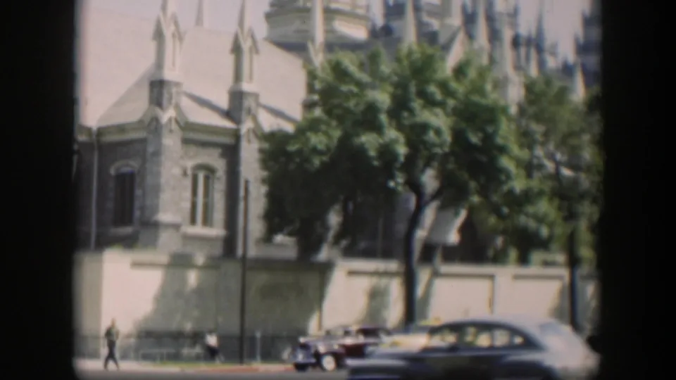1951 Wyoming 8mm frame with a small pedestrian, classic cars, trees, and a tan Gothic-style building along the street.
