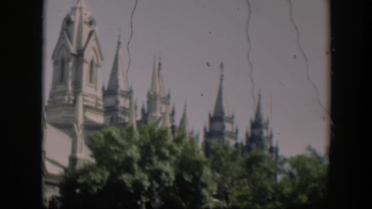 Tall pale tower and pointed spires appear behind a line of trees.