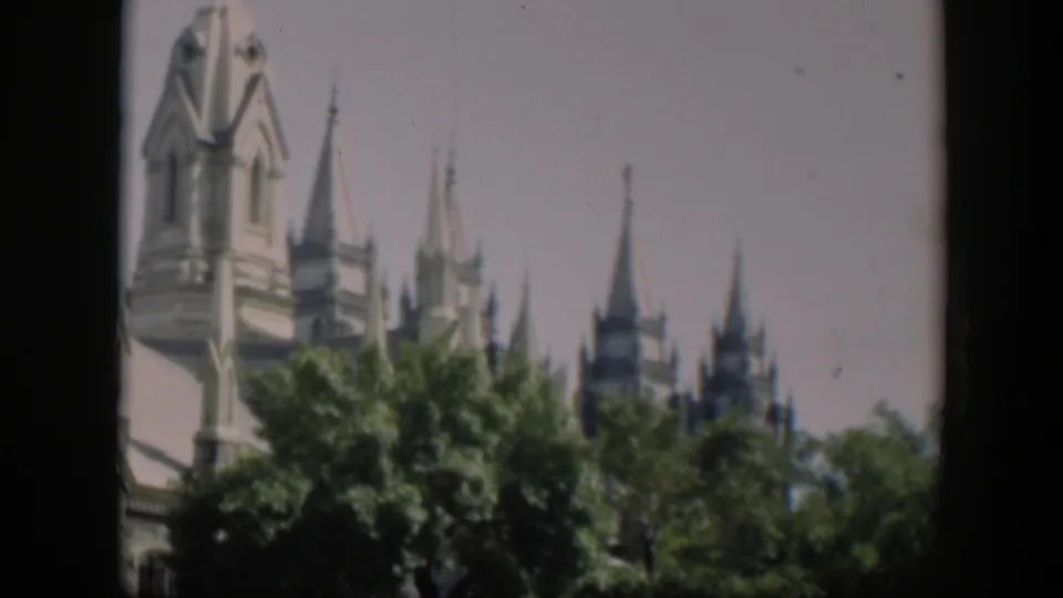 1951 Wyoming 8mm view of a pale tower, roof peaks, and spires rising behind leafy trees.