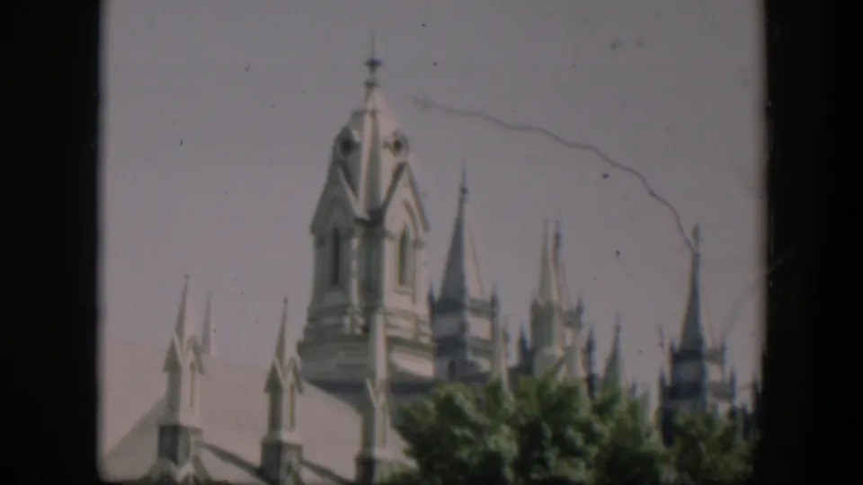 1951 Wyoming frame showing a distant pale religious tower and spires above trees, with scratches and gate edges visible.