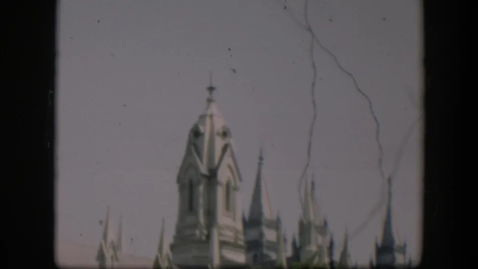 1951 home-movie frame, supplied as Wyoming, showing Gothic-style spires partly hidden by trees with visible film wear.
