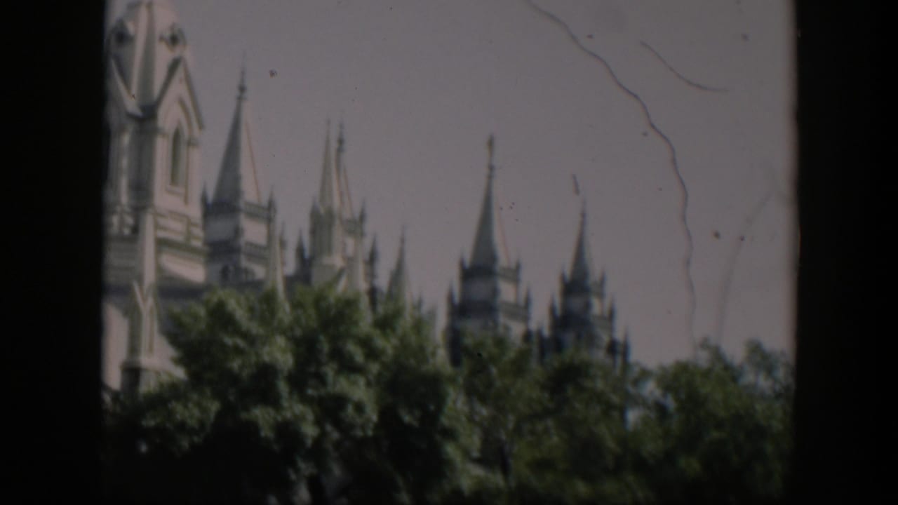 Closer view of ornate spires and treetops with dark film borders and scratches.