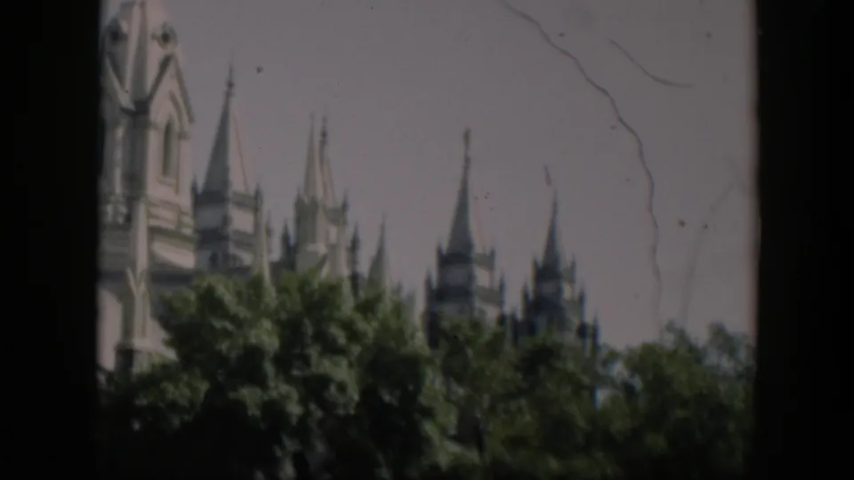 1951 8mm frame from the supplied Wyoming clip showing upper architectural towers above a dense green tree line.