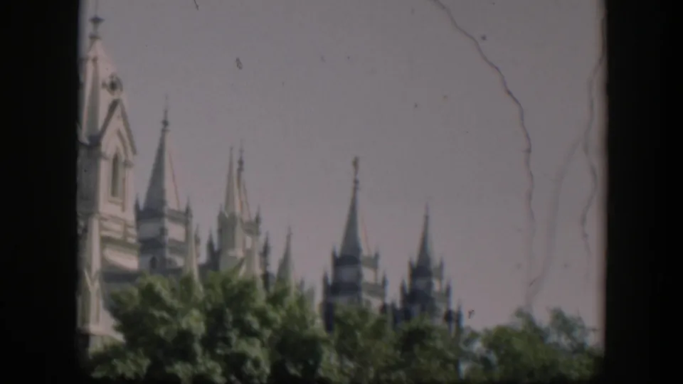 Visitor-style 1951 home-movie view of a large Gothic-style building's upper towers, partly obscured by trees.