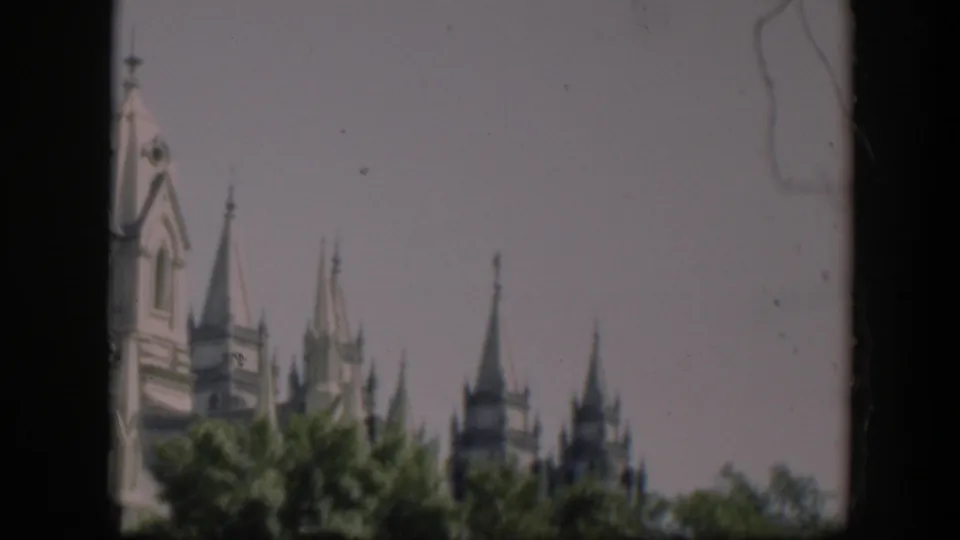 Final 1951 frame showing distant pointed spires and a tower top above trees, with soft focus and visible film wear.
