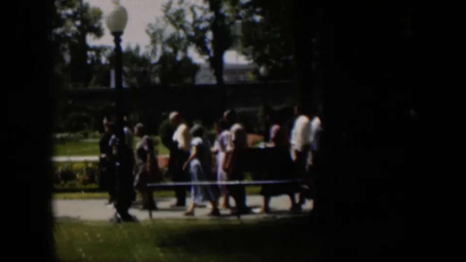 Wyoming 1951 park scene with a small group of people in mid-century clothing walking single-file along a paved path.