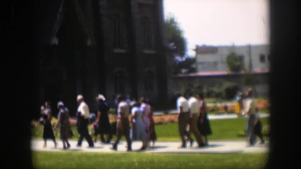 Soft 8mm frame from 1951 Wyoming showing adults walking in a line across landscaped grounds after a gathering.