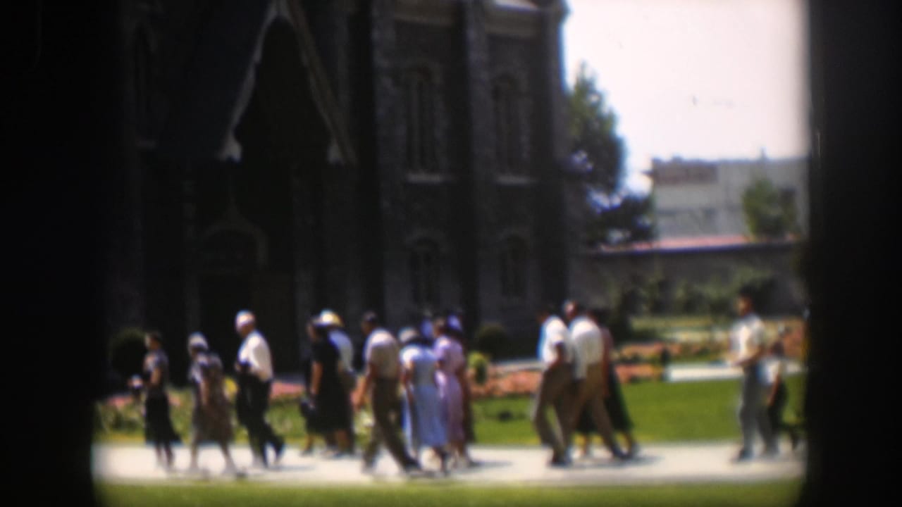 Groups of adults in mid-century clothing walk past a large stone church in Wyoming, according to the clip metadata.